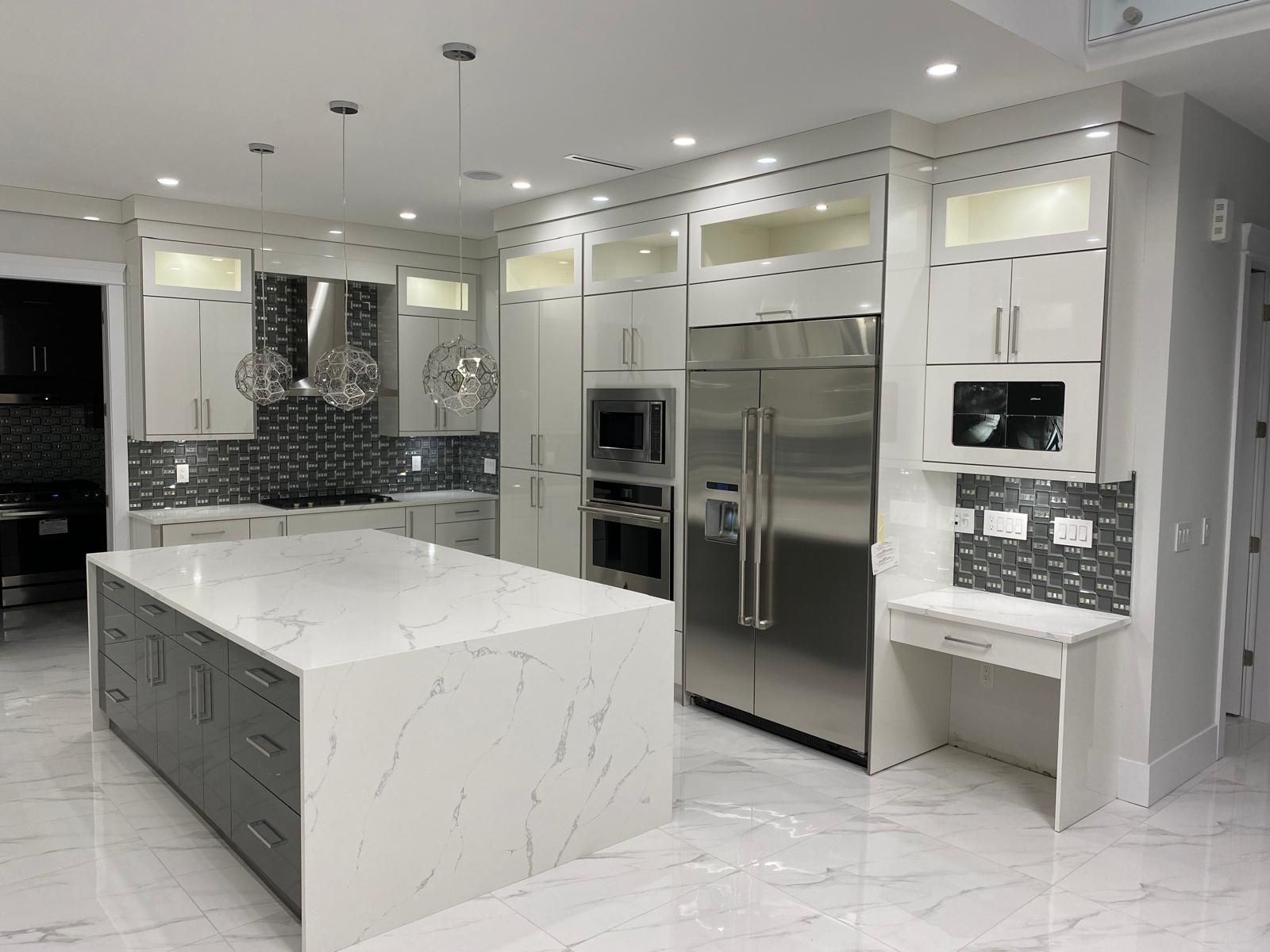 High-gloss white kitchen with a grey island and waterfall quartz top